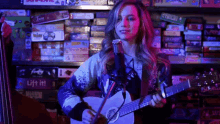 a woman is singing into a microphone while playing a guitar in front of a shelf full of board games .