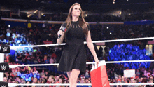 a woman in a black dress is standing in a wrestling ring holding a red bag