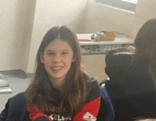 a young girl is smiling in a classroom while wearing a collegiate sweatshirt .