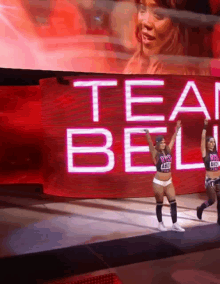 two female wrestlers are standing in front of a large screen that says team bell