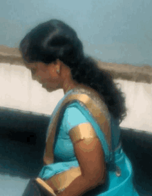 a woman in a blue and gold saree looks down at something