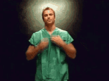 a man wearing a green scrub top is standing in a dark room .