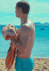 a shirtless man in blue shorts holds a towel over his chest