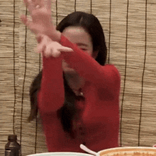 a woman in a red shirt is sitting at a table with her arms outstretched and a bowl of food .