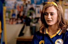 a young woman wearing a blue and yellow soccer jersey is standing in a room .