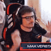 a man wearing headphones and glasses is sitting in a chair with a sign that says max versta in front of him