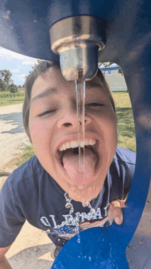 a young boy drinking water from a fountain wearing a shirt that says liberty