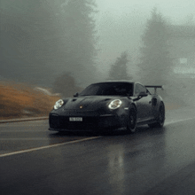 a black car is driving down a foggy road with trees in the background