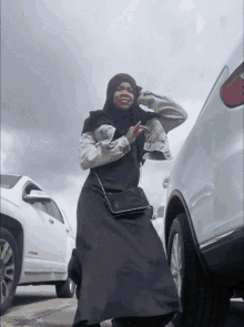 a woman in a hijab is standing in front of a white suv