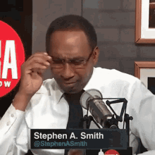 a man in a white shirt and black tie is sitting in front of a microphone with a sign that says stephen a.