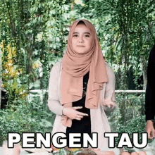 a woman wearing a hijab is standing in front of a table with food and the words pengen tau written on it .