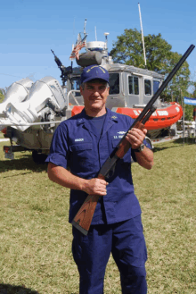 a man in a us coast guard uniform is holding a shotgun in front of a boat