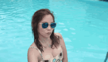 a woman in a bathing suit and sunglasses is standing in a pool