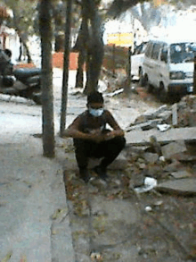 a man wearing a face mask is squatting on the sidewalk .