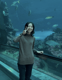 a woman giving a peace sign in front of a large aquarium