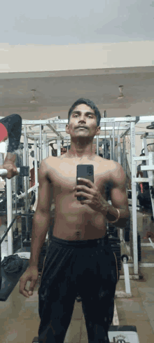 a shirtless man takes a selfie in a gym