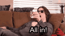 a woman is laying on a couch drinking a glass of water and saying " all in "