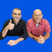 a man in a red shirt gives a thumbs up next to a man in a black shirt