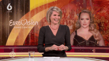 a woman sitting at a desk with a glass of water in front of a sign that says eurovision song contest