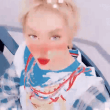 a woman with blonde hair and red lips is wearing a blue and white shirt and necklace .