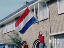 a man in a red shirt is holding a red white and blue flag in front of a brick building