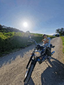 a man sitting on a motorcycle on a dirt road with the sun shining brightly behind him