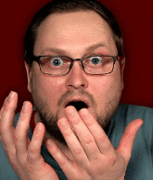 a man with glasses and a beard is covering his mouth with his hands