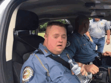 a police officer with down syndrome is sitting in a car holding a bottle of water .