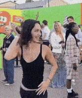 a woman in a black tank top is standing in front of a green wall .