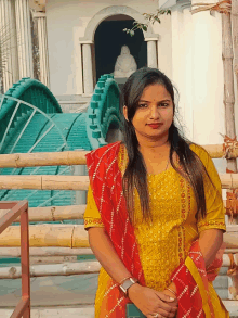 a woman in a yellow top and red scarf stands in front of a statue