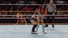 two women are wrestling in a ring while a referee stands behind them .