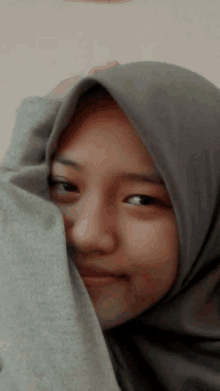 a girl wearing a gray hijab covering her face with her hand