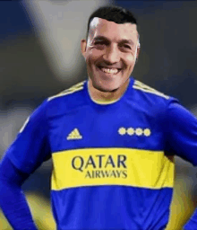 a soccer player wearing a blue and yellow qatar airways shirt is smiling .