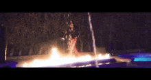 a woman in a long dress is standing in front of a pool of fire .