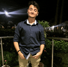 a young man in a blue shirt and khaki pants stands in front of a railing