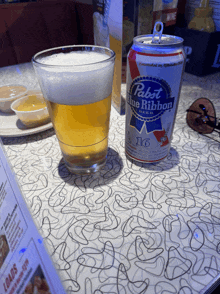 a can of pabst blue ribbon beer sits next to a full glass