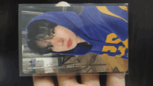 a person is holding a photo of a person wearing a blue hoodie with the number 55 on it