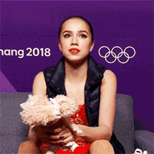 a woman is sitting on a couch holding a stuffed animal in front of a purple wall with the year 2018 on it