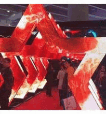 a group of people are standing in front of a large red and white triangle on a red carpet .