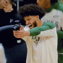 a man with curly hair and a beard is holding a camera and laughing while standing on a basketball court .