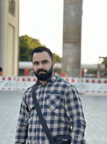 a man wearing a plaid shirt and a black messenger bag with the word eastpak on it