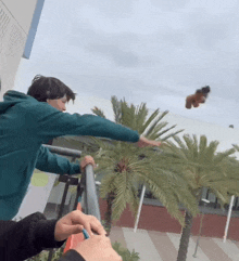 a man in a green hoodie reaches out to catch a balloon flying in the air