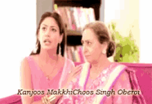 two women are sitting on a couch and the name kanjoos is on the bottom