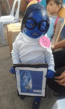 a little girl is dressed as sadness from inside out and holding a picture of sadness .