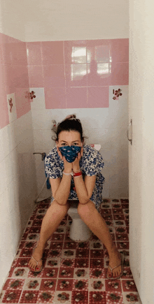 a woman wearing a mask sits on a toilet in a bathroom