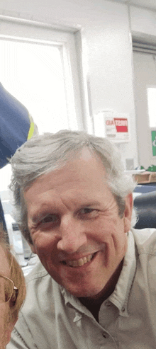 a man with gray hair smiles in front of a caution sign