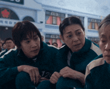 a woman in a green jacket with the number 120 on it sits next to another woman