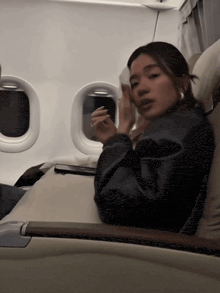 a woman in a leather jacket sits in an airplane