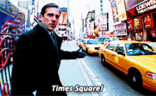 a man in a suit and tie is standing in front of a busy street with taxis and a sign that says times square