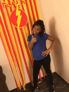 a young girl giving a thumbs up in front of a wall with the word flash on it